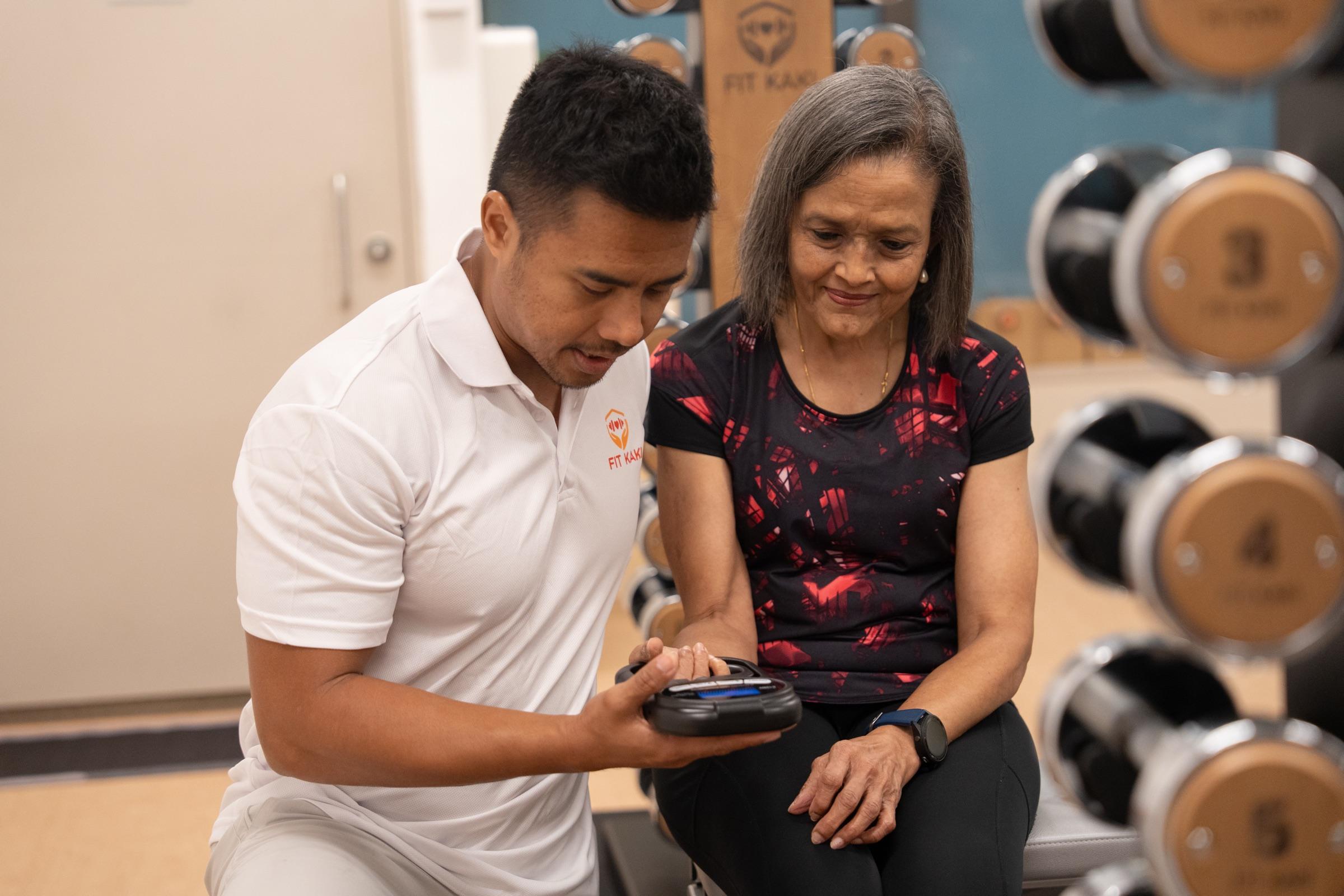 A Fit Kaki coach guiding a senior through a grip strength check, one on one