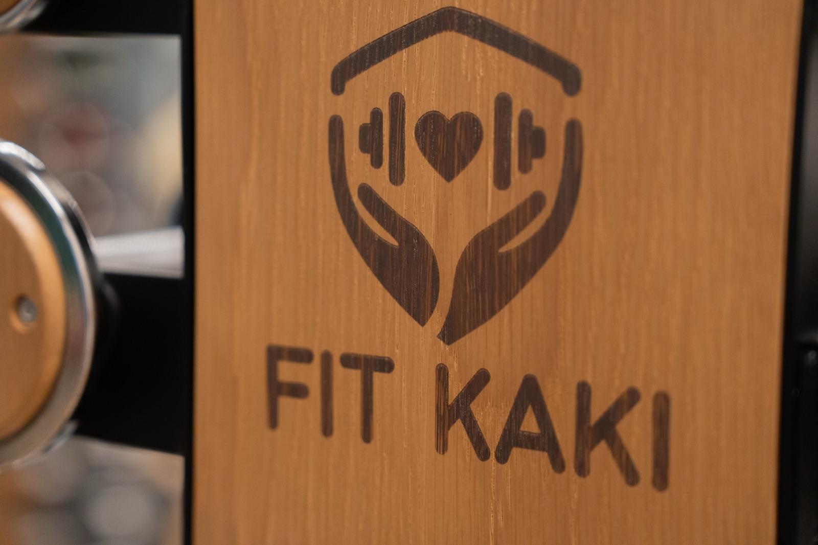 The Fit Kaki emblem — hands holding a dumbbell and heart — engraved on the studio's wooden equipment
