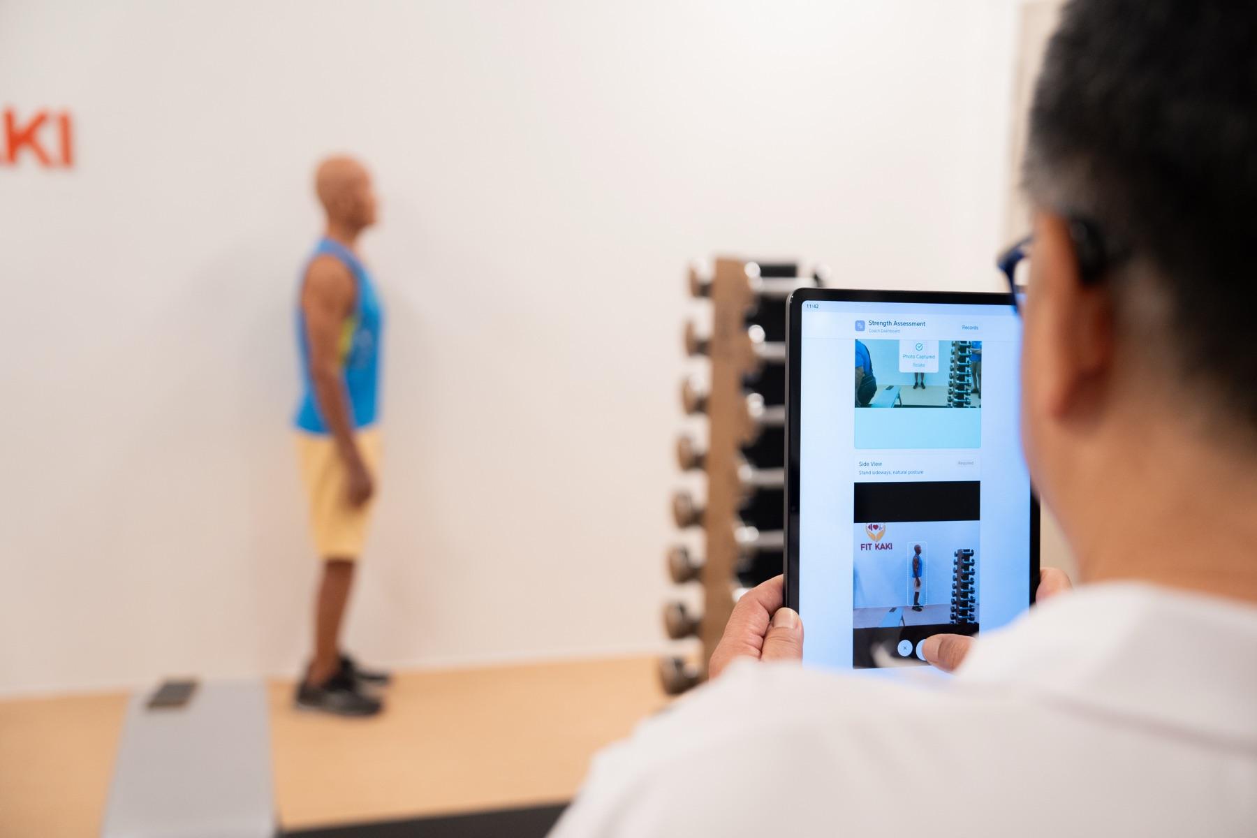 A Fit Kaki coach capturing a senior's posture snapshot on a tablet during a Strength Age Assessment at the Eunos studio