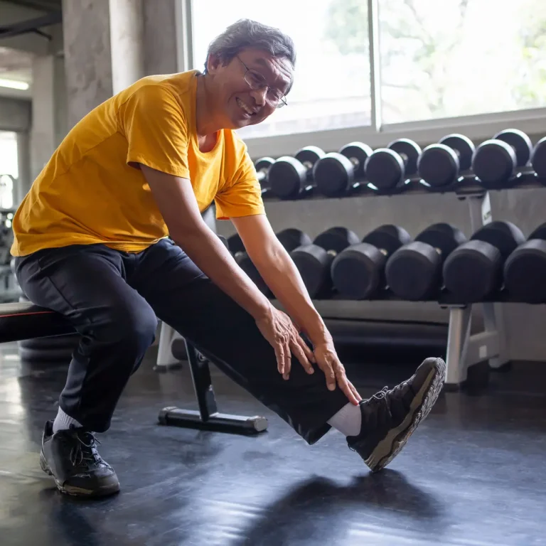 Senior asian sport man stretching his leg  in fitness gym . elder male exercising ,  working out , training , healthy ,Retirement , older, looking camera